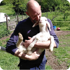 Allevatore che tiene in braccio un agnellino in un prato verde
