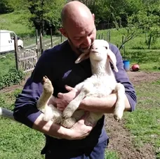 Allevatore che tiene in braccio un agnellino in un prato verde